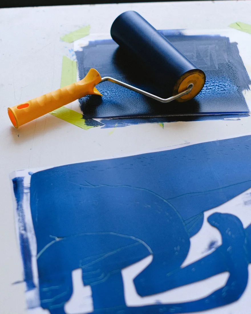 Esténcil y rodillo con tinta sobre una mesa de trabajo, vistos desde arriba