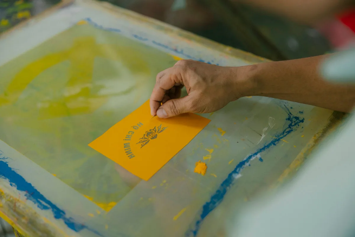 Manos sujetando una hoja recién impresa con tinta plana sobre una mesa de taller de impresión